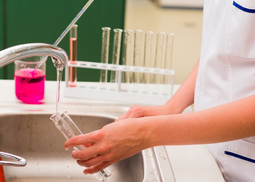 pessoa fazendo limpeza de pipetas em laboratório em água corrente