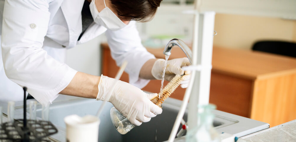 pessoa realizando a limpeza de vidrarias (proveta) em laboratório com o auxílio de uma escova