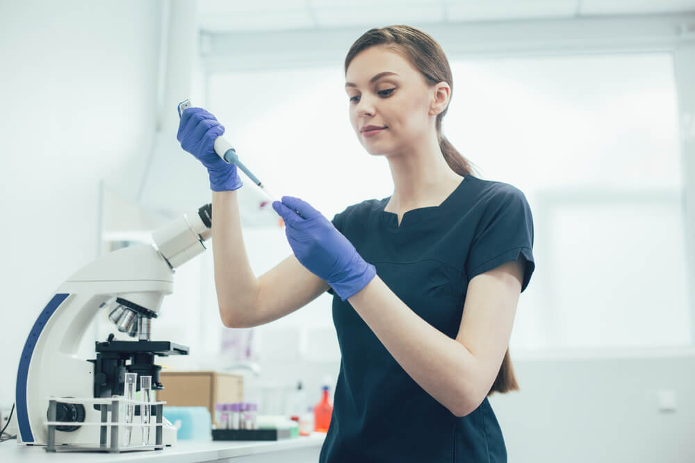 mulher em um laboratório de análises clínicas pipetando com o auxílio de uma micropipeta
