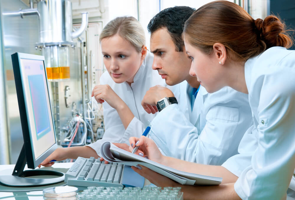 colegas de trabalho (duas mulheres e um homem) em um laboratório fazendo um planejamento estratégico para laboratório de análises clínicas em computador