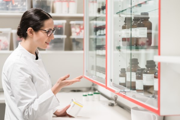 Controle de estoque no laboratório - mulher de jaleco olhando para frascos de reagentes catalogados em estoque no laboratório.
