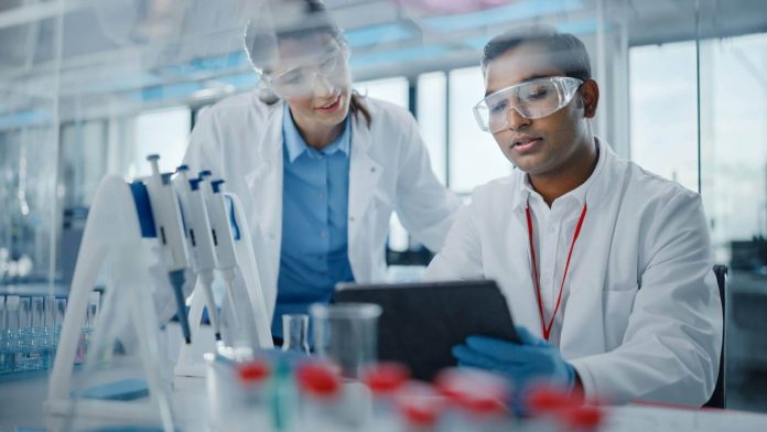 Eventos para laboratórios - Cientistas olham para resultados em tablet na bancada de um labratório com pipetadores e outros equipamentos.