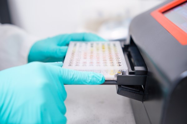 Cientista colocando microplacas em equipamento para realização de PCR.