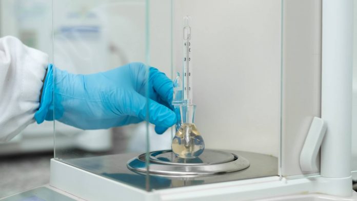 Cientista afere a temperatura de amostra com termômetro químico no laboratório.