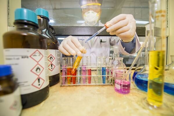 Cientista transfere líquido para tubo de ensaio em capela de exaustão no laboratório.